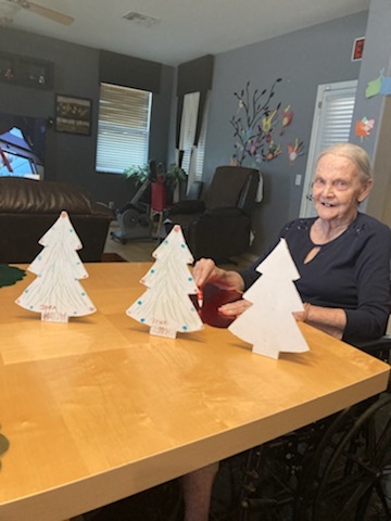 An elderly woman enjoys a festive table adorned with decorative Christmas trees.