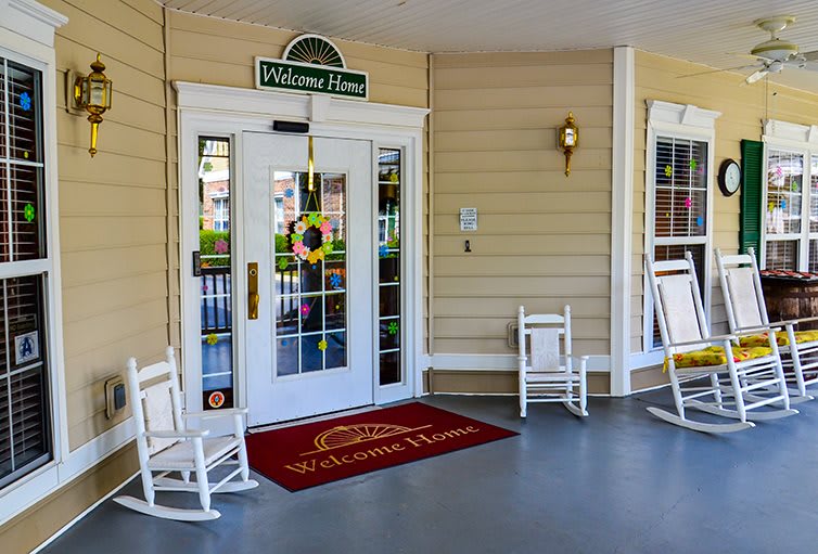 A cozy porch entrance features a welcome mat, double doors, and rocking chairs.