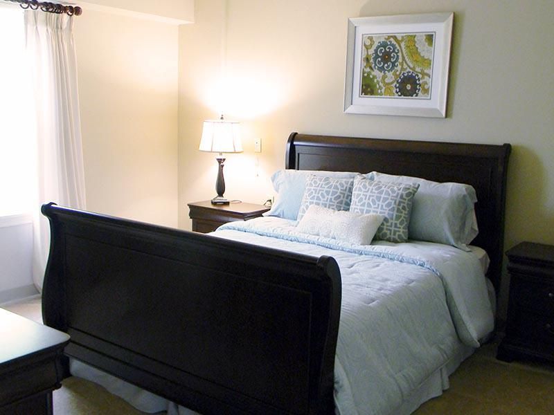 A cozy bedroom with a neatly made bed, a lamp on the bedside table, and artwork on the wall.