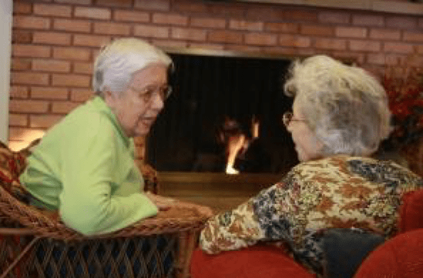 Two elderly individuals engaged in a conversation by the fireplace.
