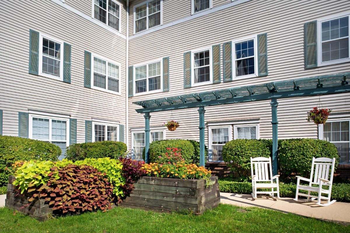 A well-maintained garden area in front of an apartment building with a bench and lush greenery.
