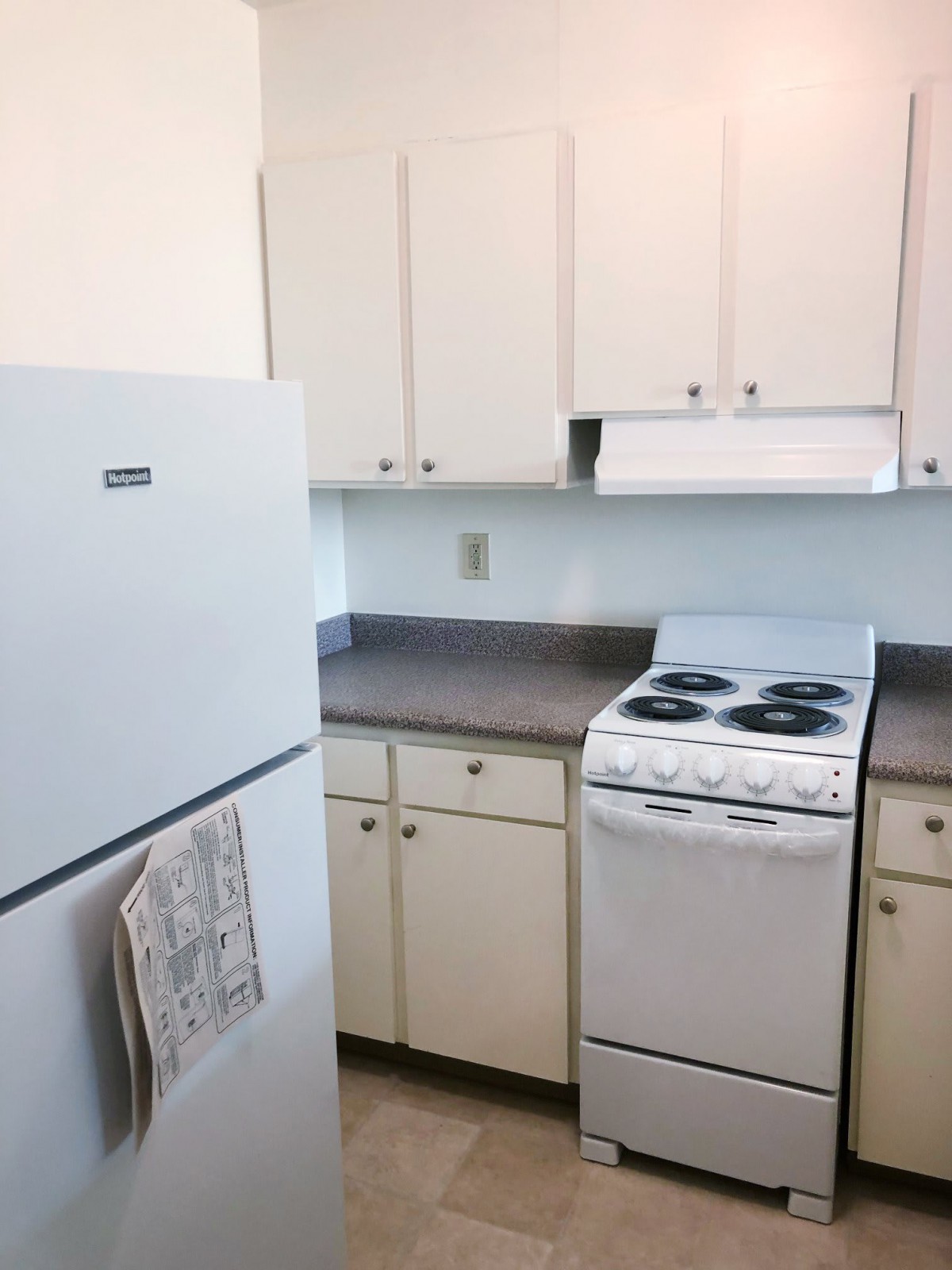 A compact kitchen with a refrigerator, stove, and white cabinets.