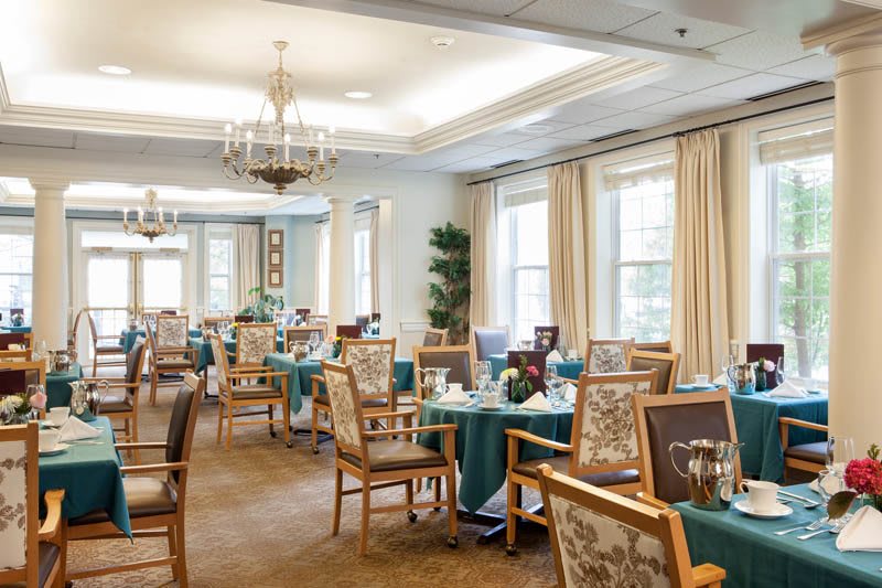 Elegant dining room with neatly arranged tables and chairs, complemented by chandeliers and large windows.