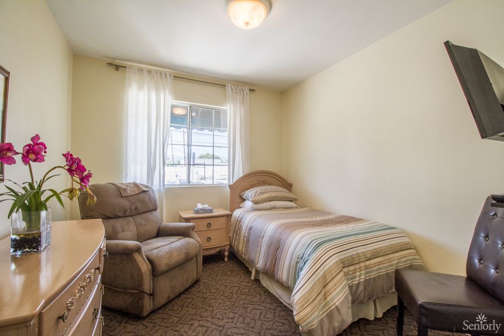 A cozy bedroom with a single bed, armchair, and natural light coming through the window.