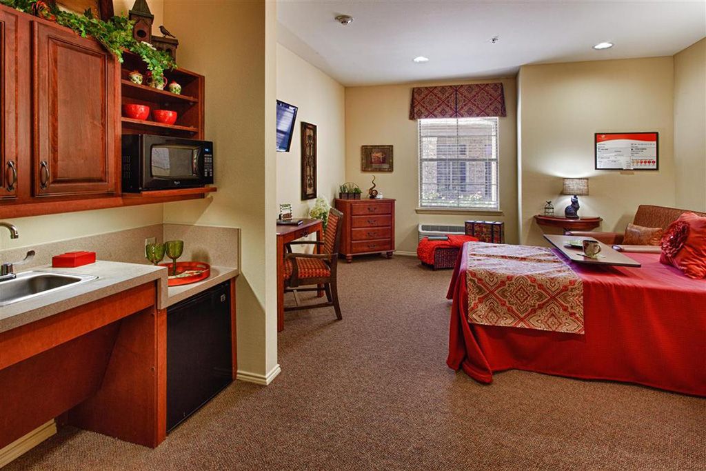 A cozy bedroom interior featuring a bed, desk, and small kitchenette.