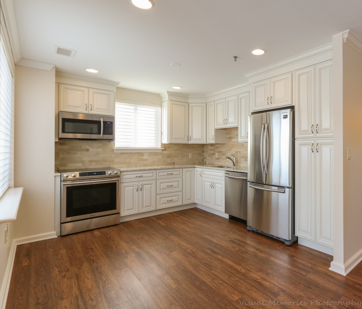 A modern kitchen with white cabinets and stainless steel appliances, featuring wooden flooring.