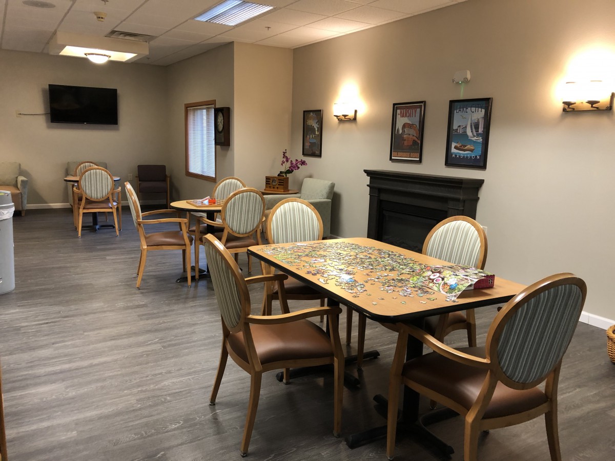 A cozy lounge area with tables and chairs, featuring a puzzle in progress and decor including a fireplace and wall art.