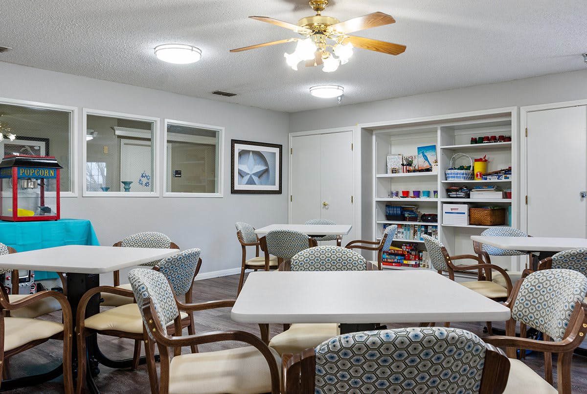 A cozy community room with tables, chairs, and a bookshelf.