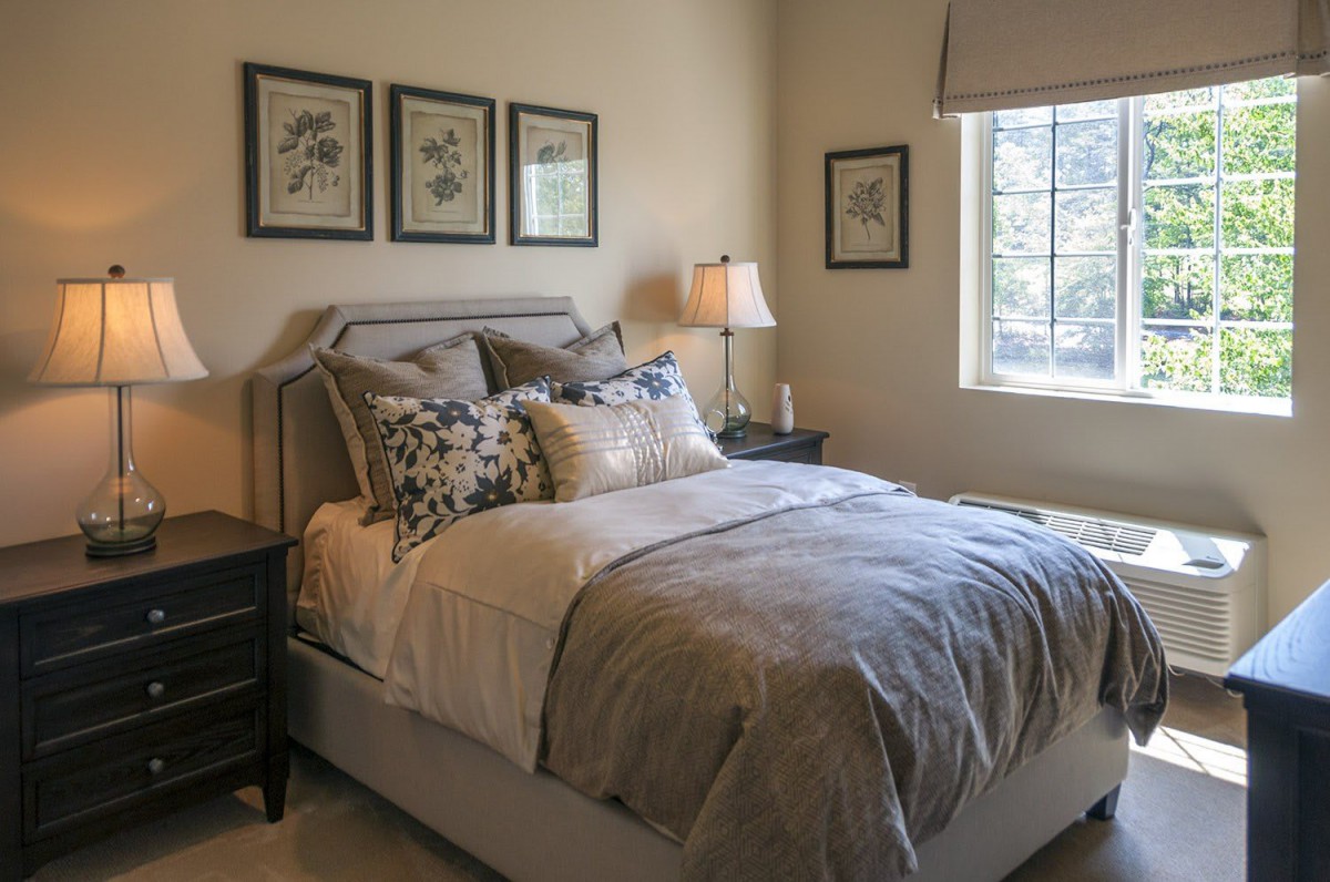 A cozy bedroom with stylish decor, featuring a neatly made bed, artwork on the wall, and natural light from a window.