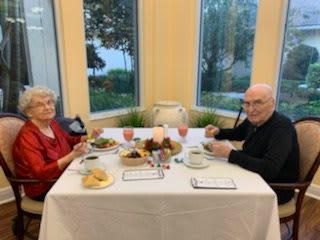 An elderly couple enjoying a meal together at a table with window views.