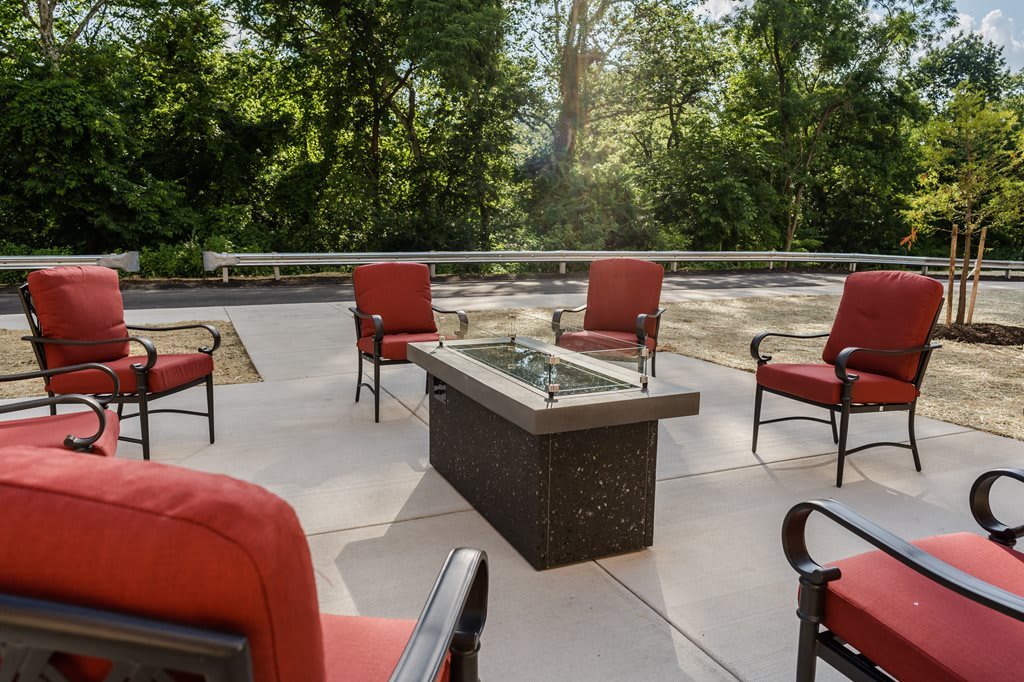 An inviting outdoor patio with red cushioned chairs surrounding a central fire pit, set against a backdrop of lush trees.