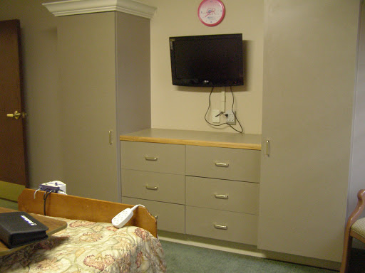 A cozy room featuring a television mounted on the wall, a dresser with drawers, and a wall clock.