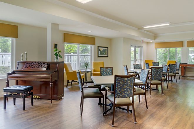 A bright dining area with tables, chairs, and a piano.