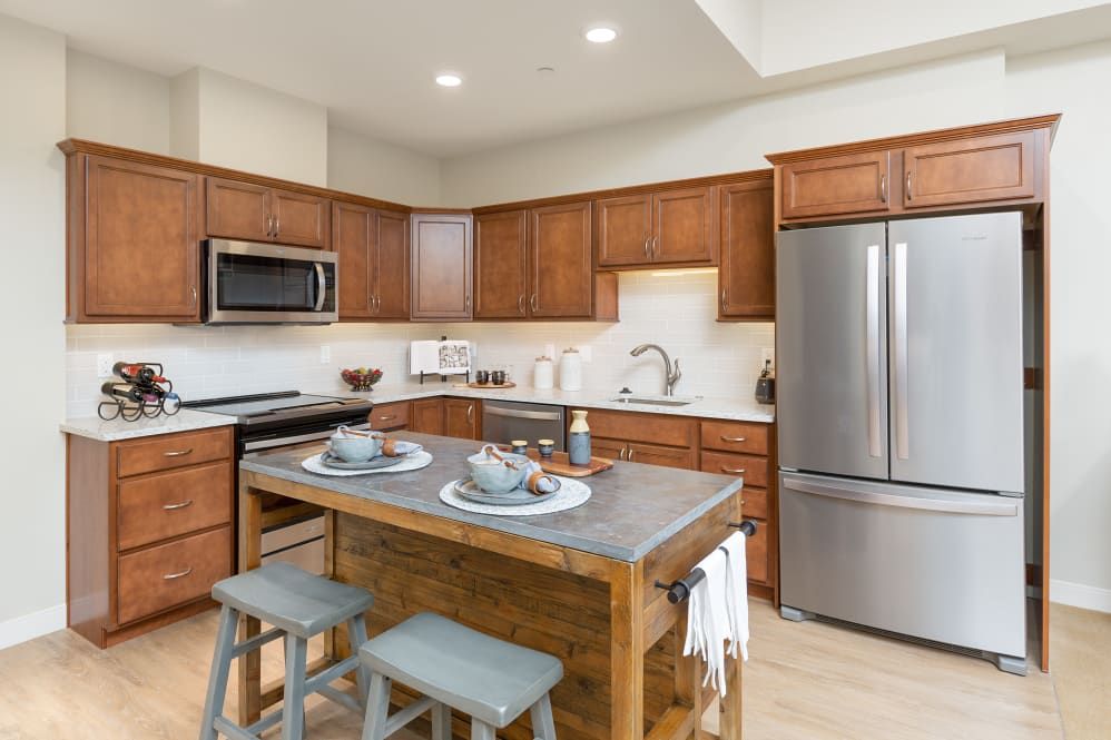 A modern kitchen featuring a central island with stools, stainless steel appliances, and wooden cabinetry.