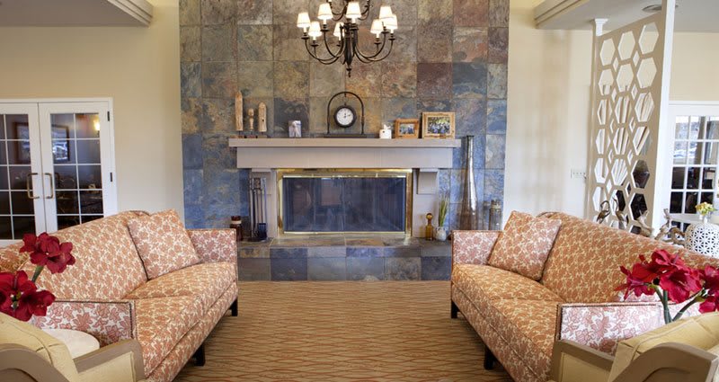 A cozy living room featuring a stylish fireplace with decorative items on the mantel and patterned sofas facing each other.