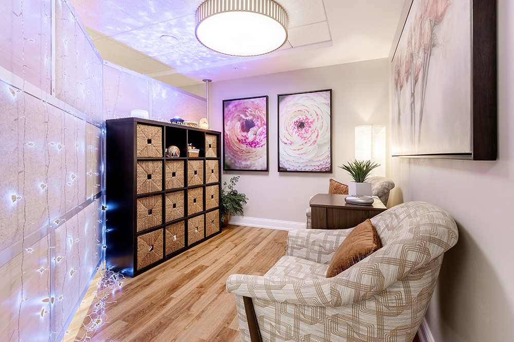 A cozy living room with stylish decor, featuring an armchair, shelving unit, and framed artwork on the walls.