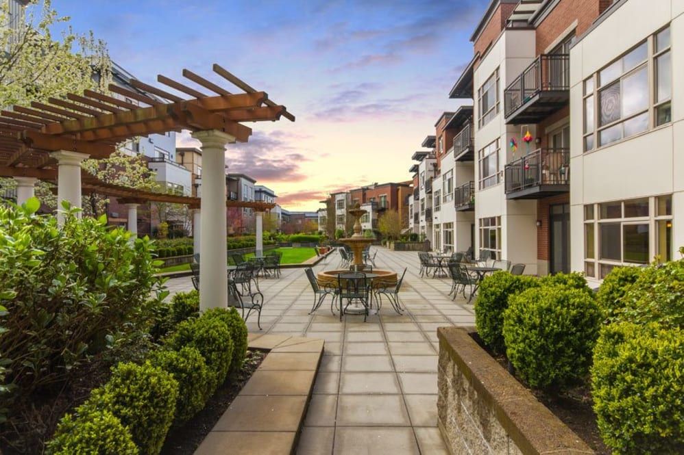 A modern apartment complex featuring an inviting outdoor patio with seating areas, beautifully landscaped and set against a stunning sunset backdrop.