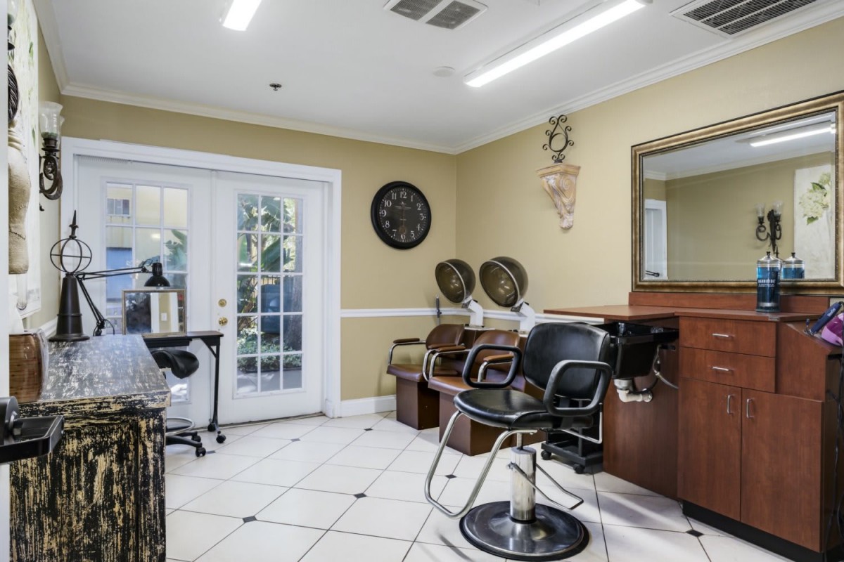 A bright and tidy salon interior with chairs, mirrors, and hair dryers.