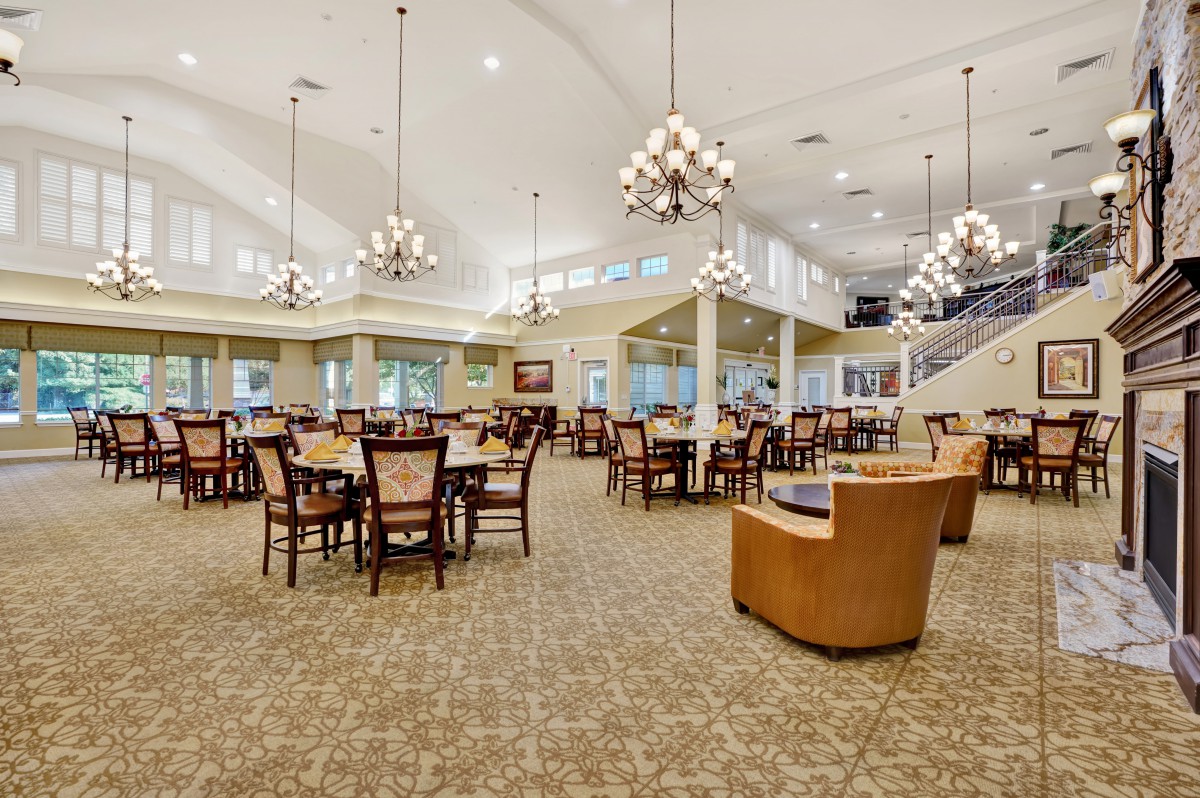 A spacious and elegantly decorated dining area featuring multiple tables and chairs, with chandeliers illuminating the room.