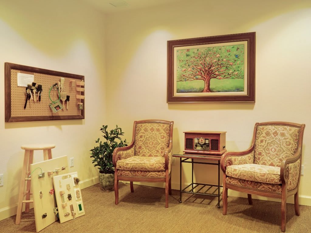 A cozy waiting room with comfortable chairs, artwork on the walls, and a small side table with decorations.
