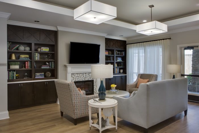 A modern living room with elegant furnishings, featuring a cozy seating area around a fireplace and TV, complemented by built-in bookshelves and stylish lighting.
