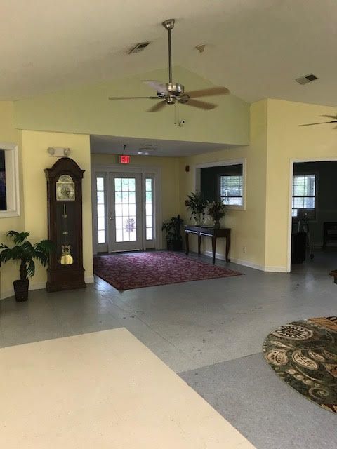 A spacious living room with a grandfather clock, plants, and a ceiling fan.