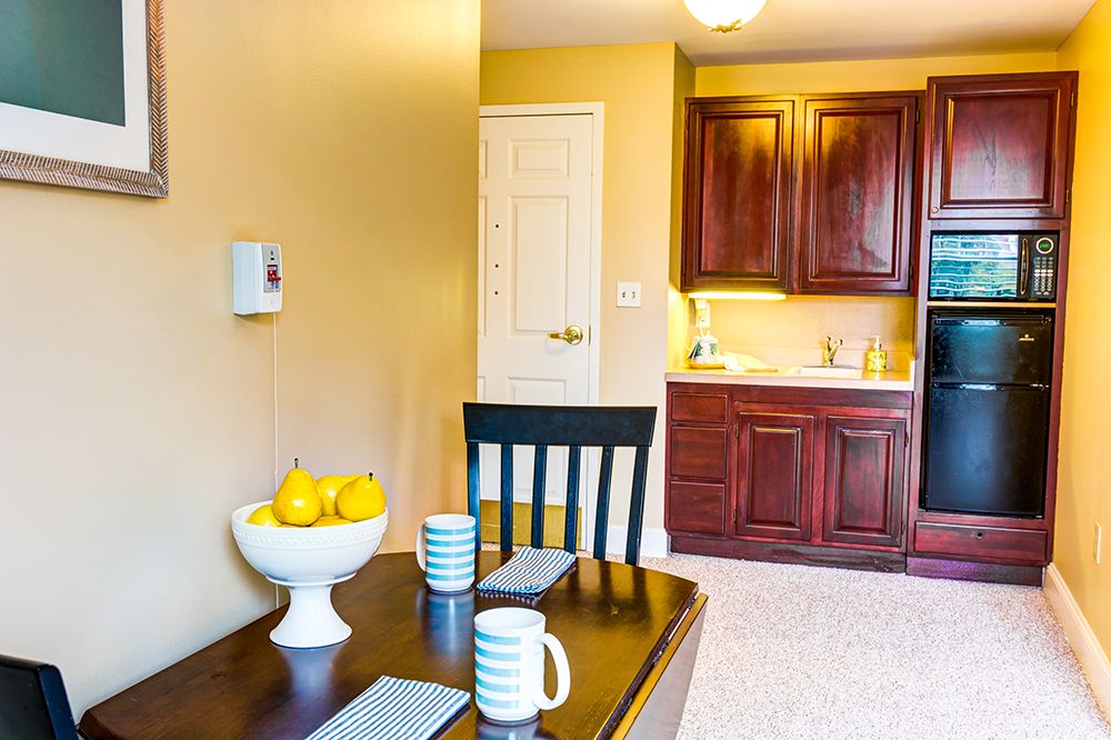 A cozy dining area next to a kitchen, featuring a dark wooden table with striped mugs and a fruit bowl filled with lemons.