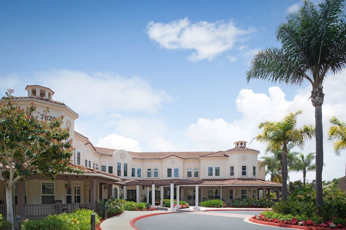 A large residential building with palm trees and a cloudy sky.