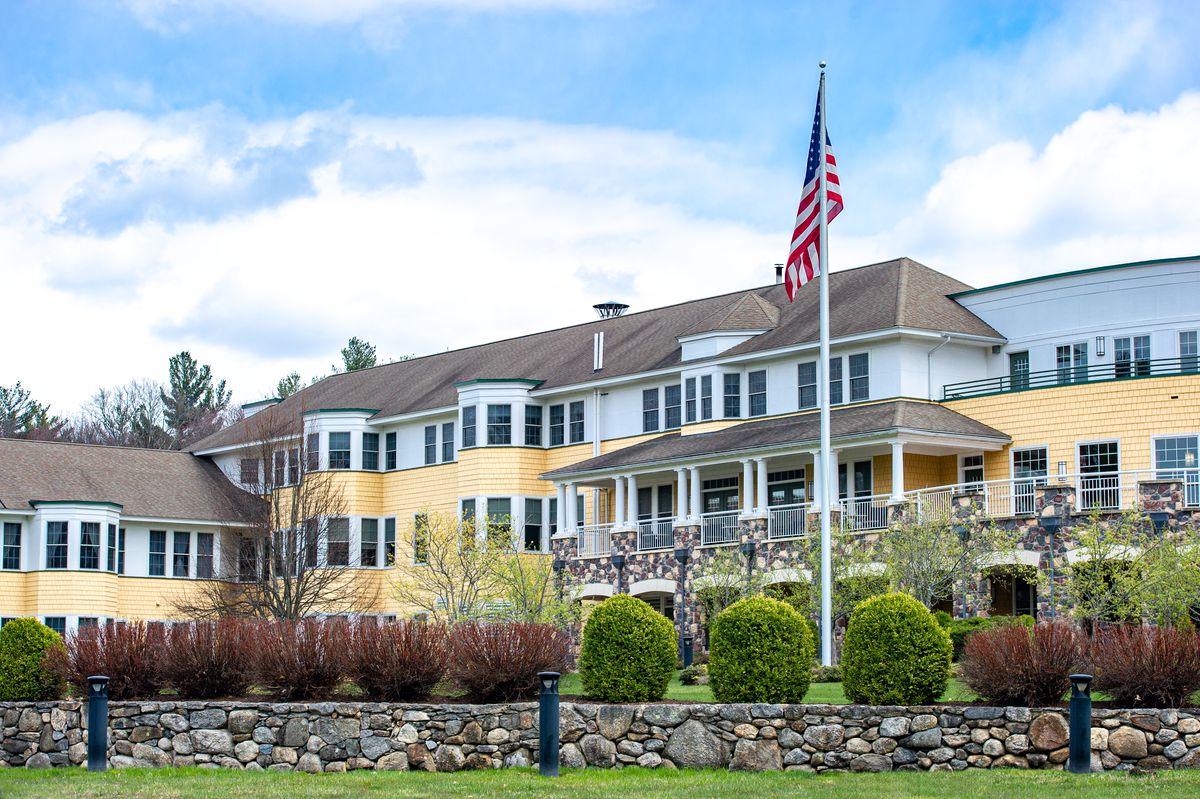 A large building with an American flag in front, surrounded by greenery.