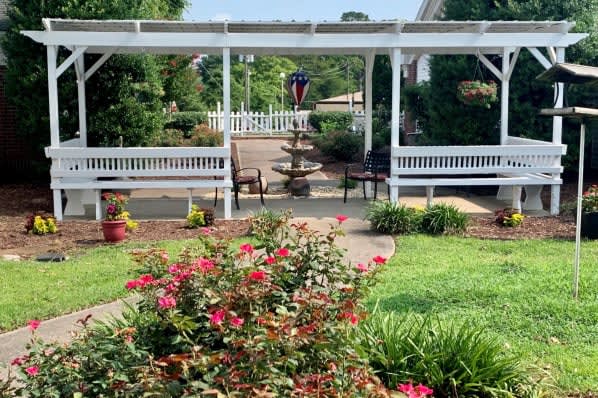 A beautiful garden with vibrant flowers, a central fountain, and white benches along a paved pathway.