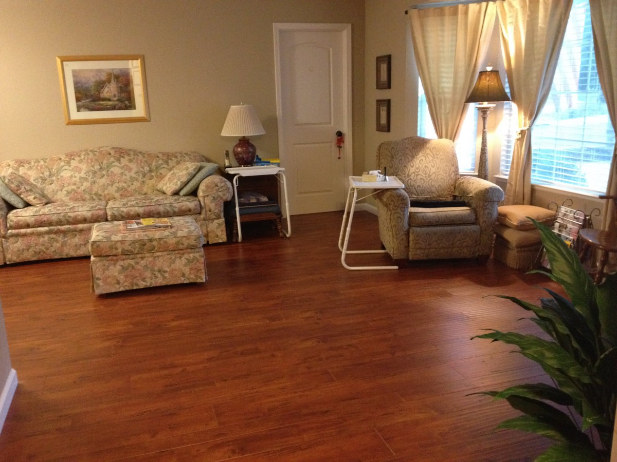 A cozy living room with a floral couch, armchair, and wooden flooring, illuminated by a lamp near the window.