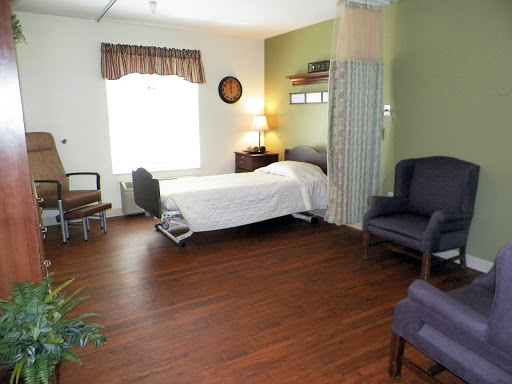A well-furnished patient room with a bed, seating area, and natural light.