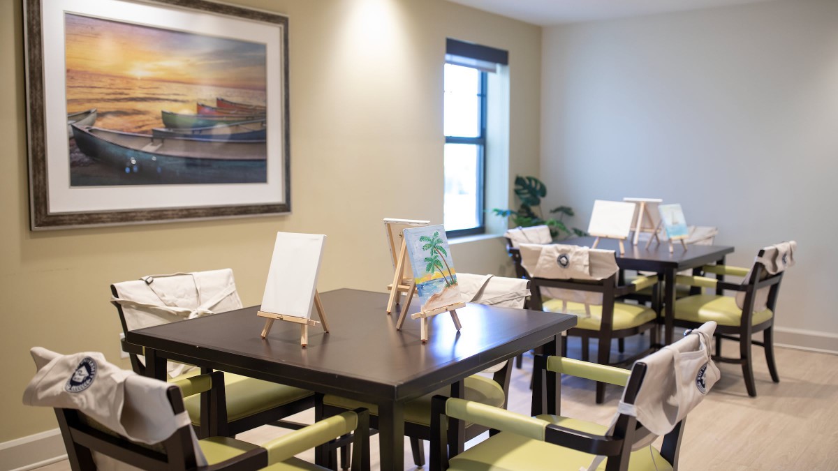 A bright indoor space featuring tables with painting easels, chairs, and wall art.