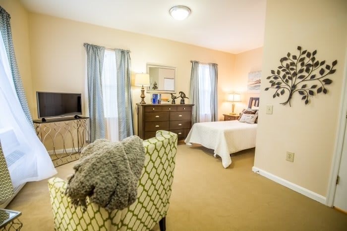 A cozy bedroom interior with a comfortable chair, bed, dresser, and decorative elements.