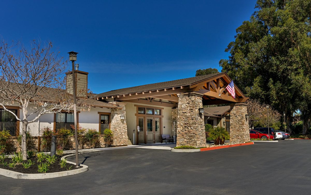 A stone building entrance with an American flag and surrounding greenery under a clear blue sky.