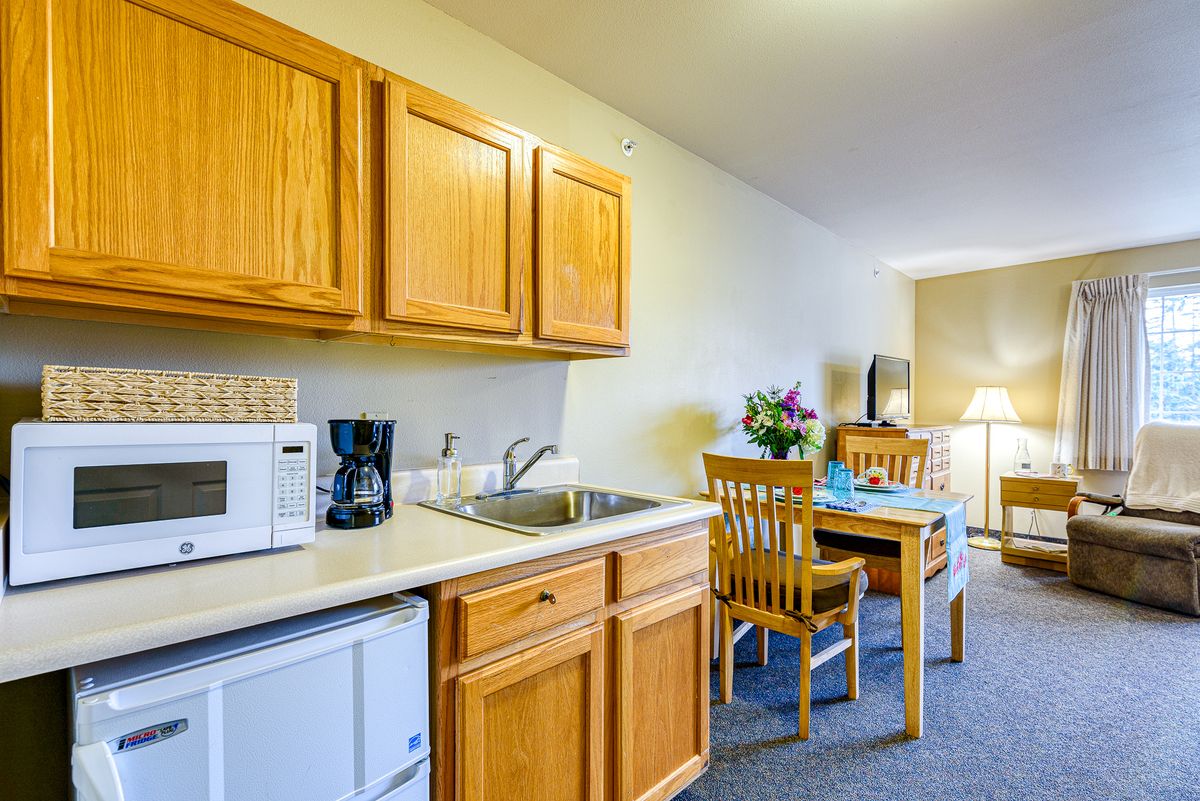 Compact kitchenette in a hotel room with wooden cabinets and a small dining area.