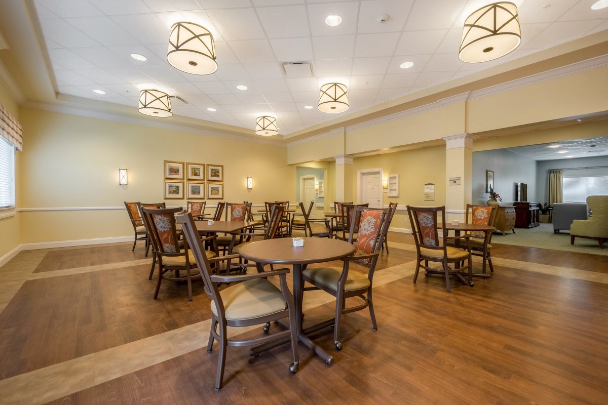 A spacious dining area with wooden tables and chairs, featuring stylish overhead lighting and a warm interior design.
