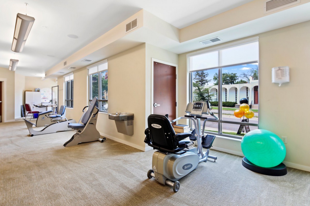 A bright gym room with exercise equipment and large windows.