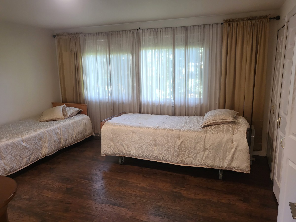 A minimalist bedroom featuring two single beds with wooden flooring and large windows covered by curtains.