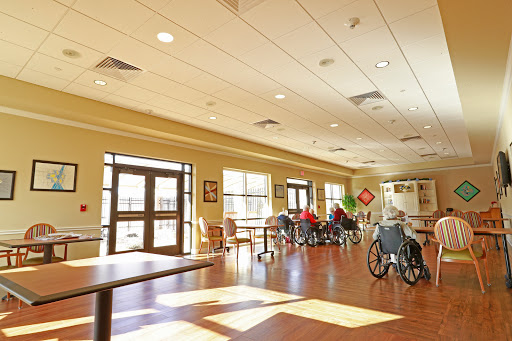 A bright and spacious common area in a nursing home, featuring several wheelchairs and ample natural light.