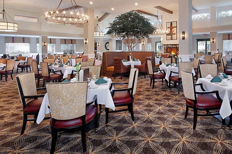 An elegant restaurant interior with neatly arranged dining tables and chairs under a large chandelier.