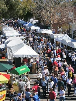A bustling outdoor festival with numerous tents and a large crowd of people.
