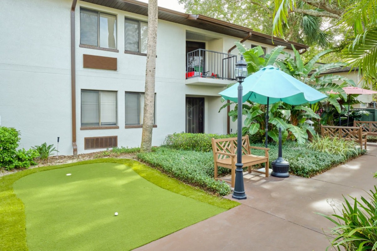 An outdoor patio area with a seating arrangement, umbrella, and well-maintained greenery in front of an apartment building.
