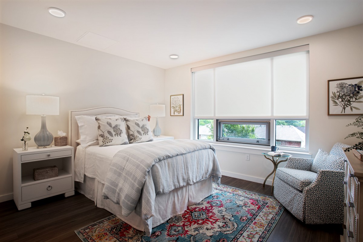 A cozy modern bedroom with ample natural light, featuring a comfortable bed and decorative carpet.