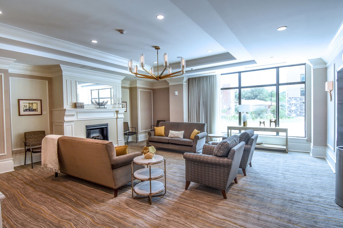 A modern, well-lit living room featuring a seating area with sofas, a central fireplace, and a chandelier.