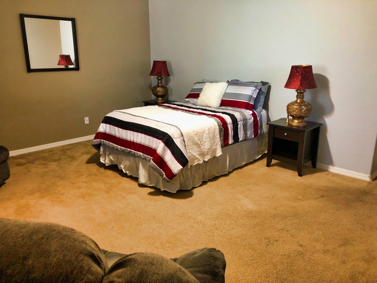 A cozy bedroom with a bed featuring striped bedding, flanked by nightstands and lamps, carpet flooring, and a wall mirror.