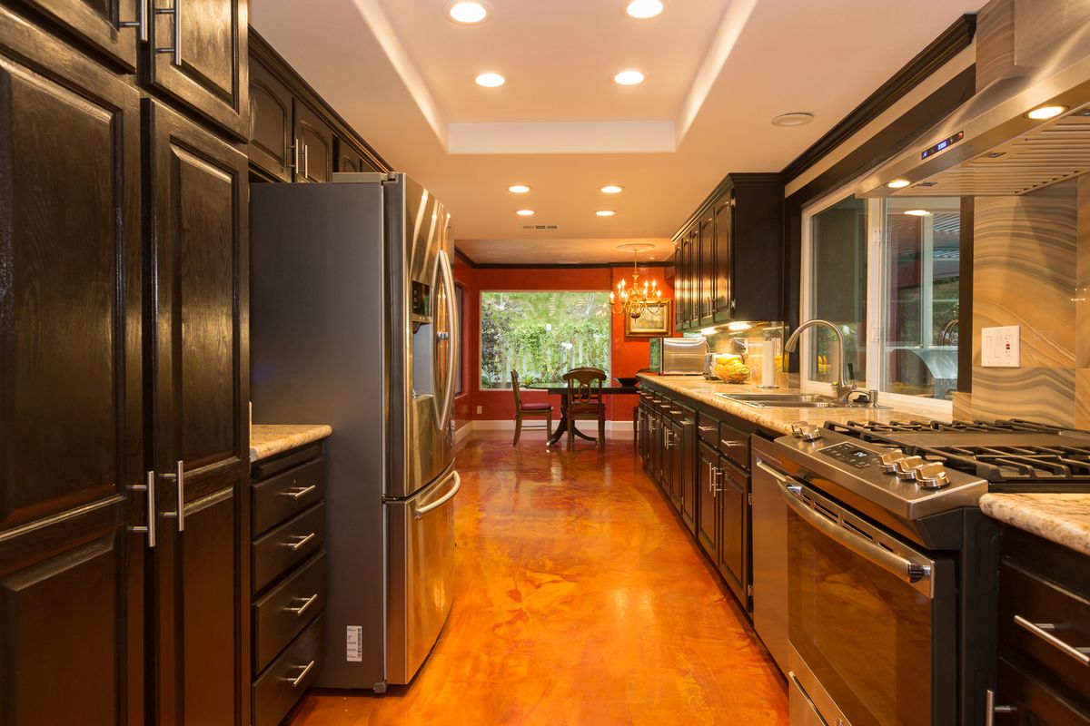 A spacious and modern kitchen with stainless steel appliances, hardwood flooring, and recessed lighting leading to a dining area.