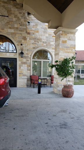 A cozy outdoor seating area in front of a stone building, featuring two chairs and a table beside a potted plant.