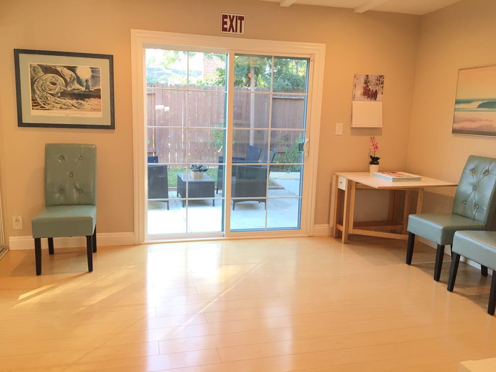A bright, minimalist room with two chairs, a desk, and a sliding glass door leading to an outdoor area.