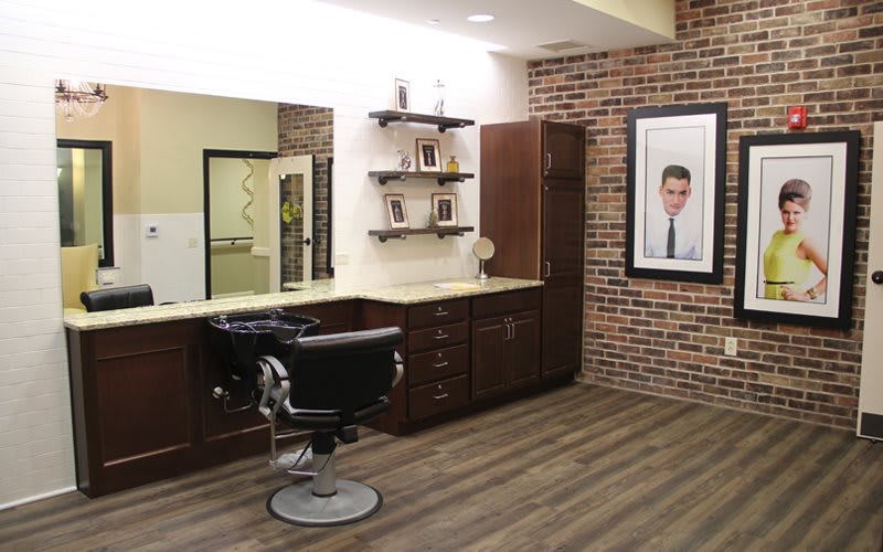 A stylish barbershop interior with a barber chair, mirrors, and shelves against a brick wall.